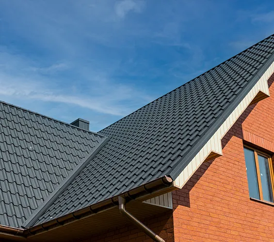 A house with a red brick wall and a gray metal roof with a clear blue sky background.