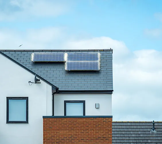 Solar panels gleam atop a modern house roof, with a mix of brick and white walls beneath the clear blue sky, offering eco-friendly energy solutions. This beautiful home stands as an ideal option for those seeking build-to-rent opportunities with comprehensive warranties.