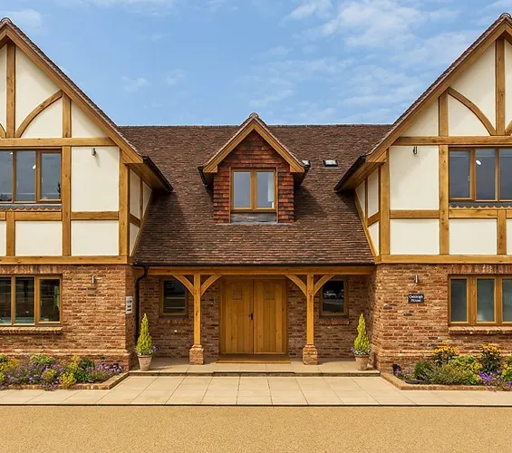 A two-story brick and timber house with a wooden front door and a small covered porch. Flower pots flank the entrance.