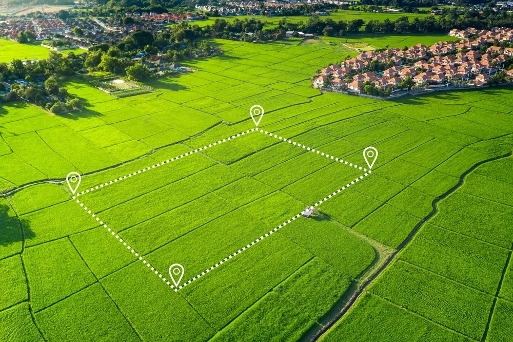 Aerial view of a green agricultural field with an outlined rectangular plot, marked by location pins, near a residential area.