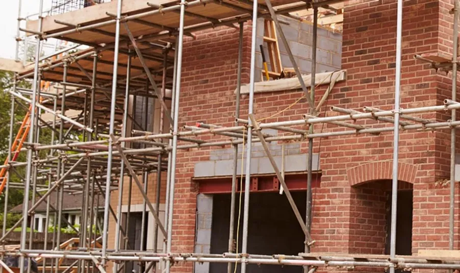 A brick building under construction, surrounded by metal scaffolding. The structure features window and door openings.