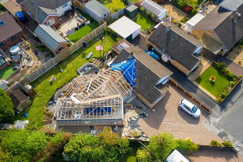 Aerial view of a house with a partially built roof next to a construction site containing building materials.