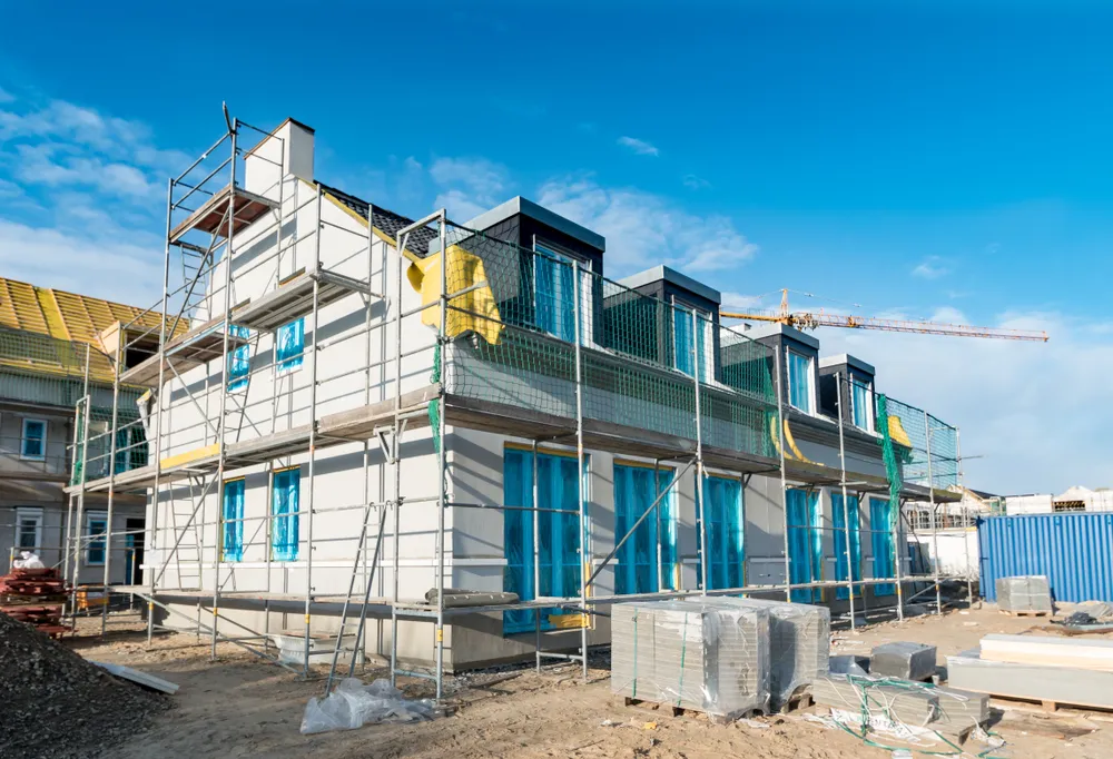 Construction site showing a multi-story building with scaffolding and materials; a crane and clear blue sky in the background.