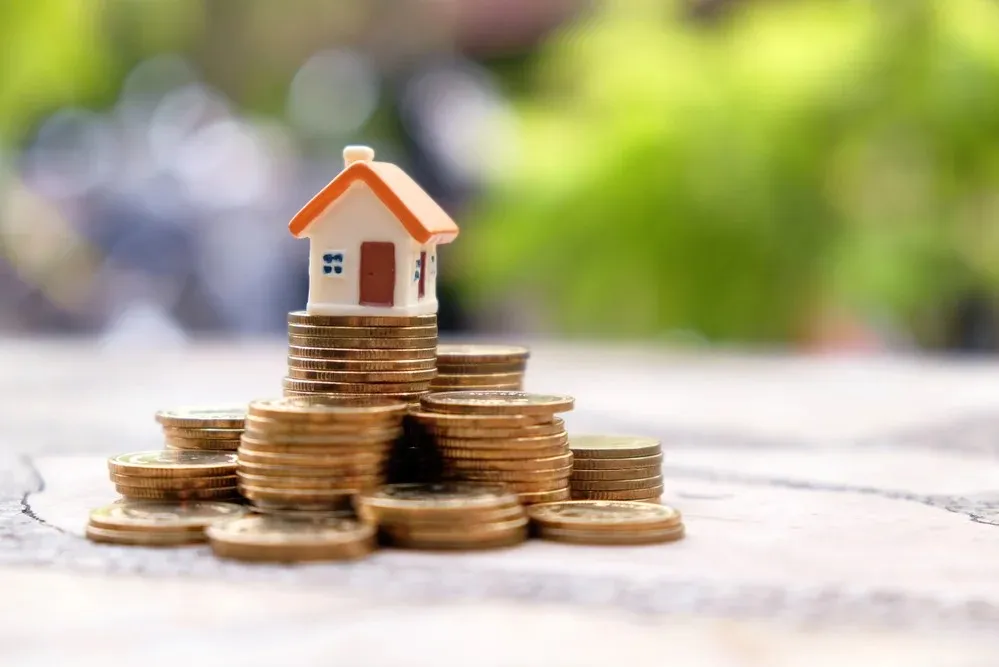 A miniature house sits atop stacked gold coins, symbolizing real estate investment and financial growth.