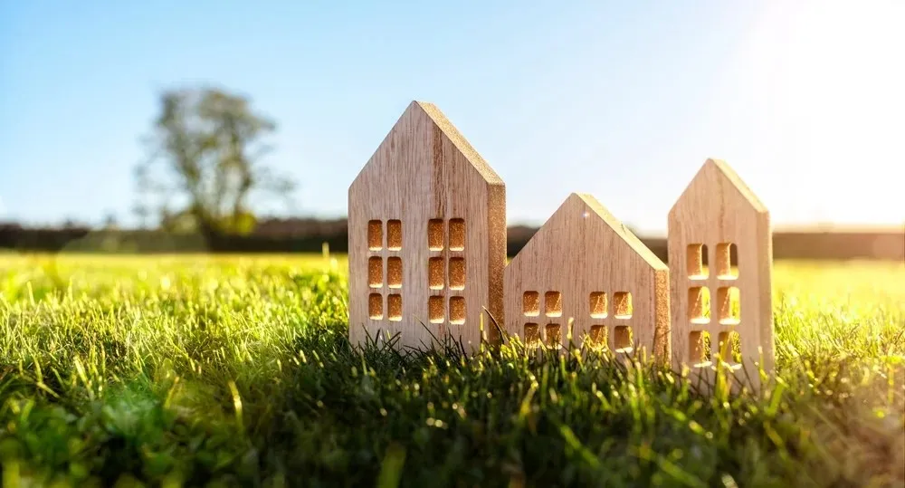 Three wooden model houses on green grass with a sunny, blue sky background.