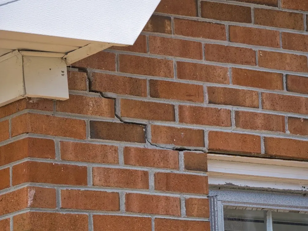 Close-up of a brick wall with clear horizontal and vertical cracks near the corner of the building and below a window.