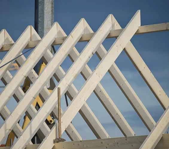 Wooden roof trusses of a building under construction, with a clear blue sky in the background.