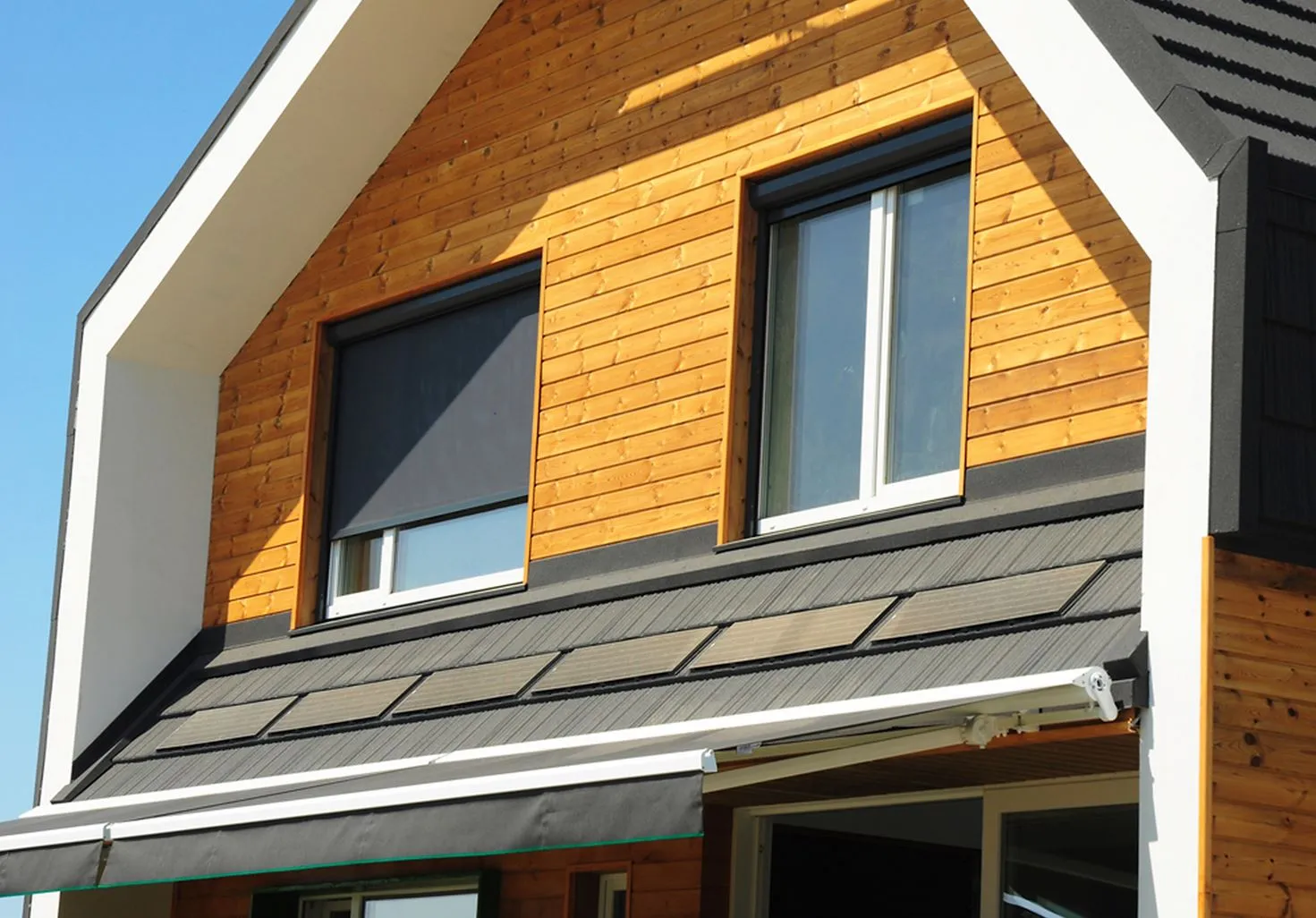 Modern two-story wooden house exterior with two windows on the top floor and an awning covering the lower level entrance.