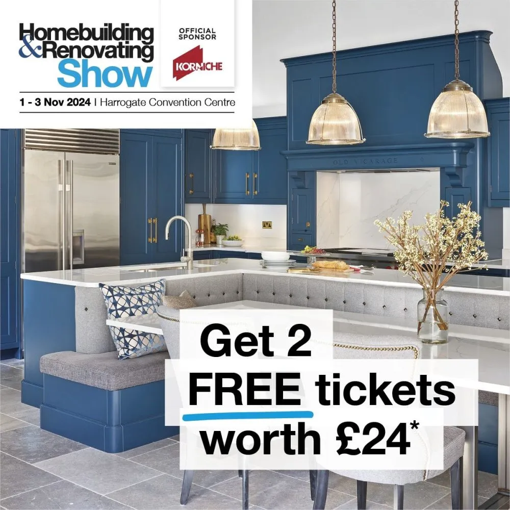 Modern kitchen with blue cabinets and a white island. Plus, enjoy peace of mind with self-build insurance and warranties. Text overlay offers two free tickets to the Homebuilding & Renovating Show.